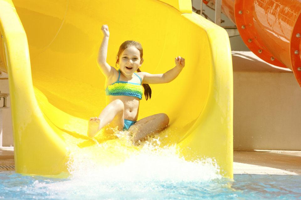 Happy young child about to splash down from a big yellow waterslide at sunny Aqualava waterpark in Playa Blanca, Lanzarote, Spain