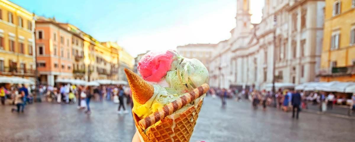 Colourful gelato in a huge cone against a backdrop of a busy street scene in Rome